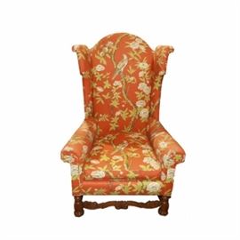 Upholstered High Back Armchair: An upholstered high back arm chair. This high back upholstered armchair features a peach background with yellow, white floral and bird pattern to the front of the chair. The back and sides of the chair feature a yellow velour fabric. The chair has rolled arms and a high winged back. The base has a chestnut satin finish with carved floral stretchers and round pedestal feet.