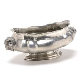 Pewter Centerpiece: A pewter centerpiece. This long oval bowl with a scalloped rim has embossed rams head to each end and sits on a pedestal foot. Marked to the underside is are two undistinguished European marks along with “95” indicating this piece is 95% tin.