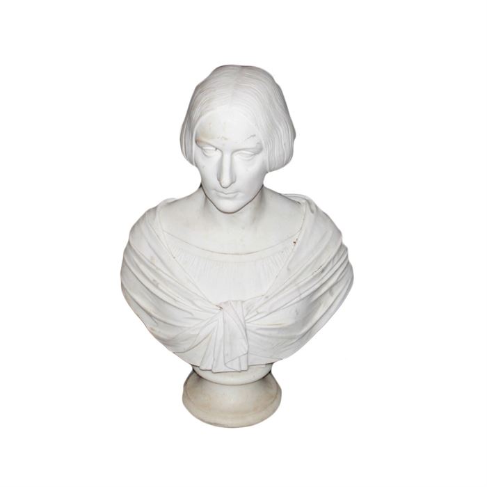 "G. Nucci F. Roma" 1857 Marble Bust of Woman: A white marble bust dated 1857. The sculpture depicts a woman with center-parted hair pulled behind her head and braided in back. The woman wears two layers of clothing including a wrap that ties at the center. The bust rests on a round pedestal. It is marked on the back “G. Nucci. F. Roma. 1857.”