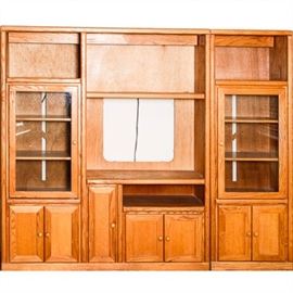 Wooden Entertainment Center: A wooden entertainment center. The entertainment center is two pieces. When put together it includes a space for a television, four shelves, two glass doors with shelving units inside, and four storage units with solid doors.