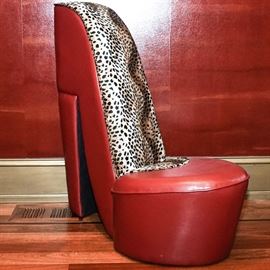 Red Leather Stiletto Heel Chair: A statement chair, shaped like a stiletto heel shoe. It is upholstered in red leather, with cheetah print upholstery on the back and seat. Piece is unmarked.