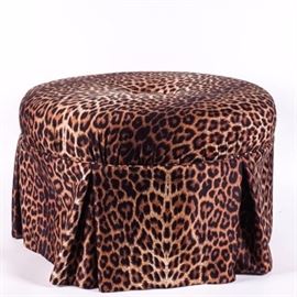 Round Leopard Print Ottoman: A round leopard print ottoman. This round ottoman features a padded top with button accent and skirted bottom in a faux leopard print upholstery. Ottoman sits on straight wooden legs.