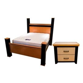 Contemporary Style Queen Size Bed, Nightstand, and Mattress Set: A contemporary style queen size bed, nightstand, and mattress set. This grouping includes the four poster bed, with a blond maple panel headboard and footboard between textured black square posts. The rails are included. Also included is the matching two-drawer nightstand. It has a blond maple top and drawer fronts, with textured black sides and square legs. A tag inside a drawer reads “Millennium”. A queen size Serta Perfect Sleeper mattress and foundation set is included.
