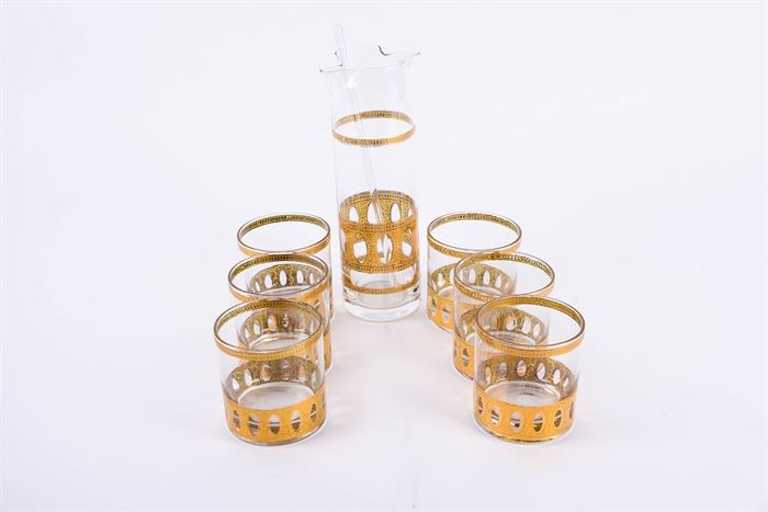 Culver Mid Century Modern Gilt Cocktail Glass Set: A set of Culver mid century modern gilt cocktail glasses. Included are six vintage glass cups and one pitcher with a stirring stick. All feature matching gilt accents with clear glass bodies. The pitcher features a fluted top and clear stirring stick.