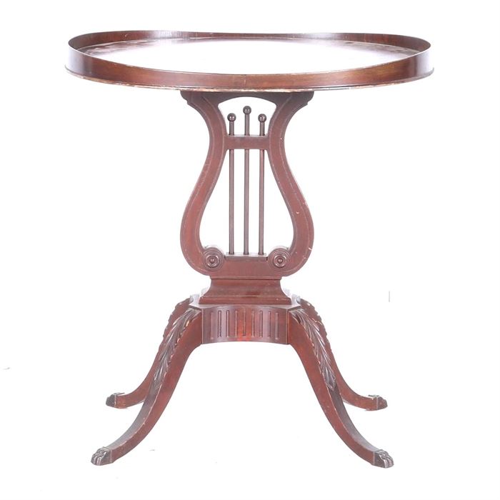 Wooden Harp Style Table: A wooden harp style table. This oval accent table has a mahogany colored stained finish. It has a raised edge to the top, carved details to the legs and petite claw feet.