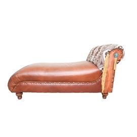 Contemporary Leather Chaise With Southwestern Accents: A contemporary leather chaise with Southwestern accents. This lounger has a fully brown leather body with Texas star fasteners. Along the single curled back is a pendant of faux turquoise and tassels. This lounger rests upon four bun feet.