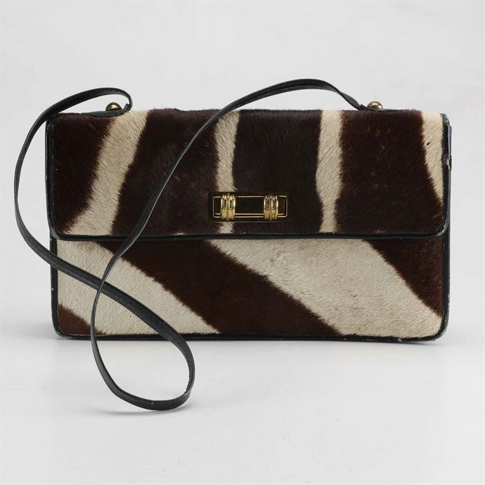 1950s Zebra Hide Handbag: A 1950s zebra hide handbag. This bag has a black leather base with the hide covering the exterior. There is a gold tone buckle along the front and brass fasteners for the shoulder strap. There is a bi-fold along the interior with a zipper along the divider.