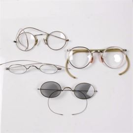 Collection of Antique Eyeglasses: A collection of antique eyeglasses. Featuring four pairs of antique eyeglasses with metal frames. One pair of glasses has tinted lenses. Two pairs of glasses have maker’s marks on the lenses. Markings on metal frames include “10 12 K GF AAA”, “FUL-VUE”, and a capital A within a capital C logo.