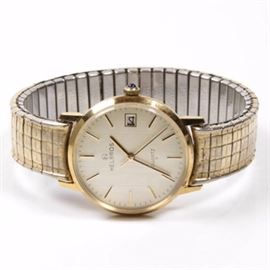 Men's Helbros Wristwatch: A men’s Helbros wristwatch. Featuring a men’s watch with a white face marked “Helbros Quartz”. The watch face has a date function and three gold colored hands. The back of the face is marked “Base Metal Bezel Stainless Steel”. The band and face surround are gold-tone metal.