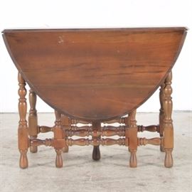 Walnut Top Gate Leg Table: A walnut top gate leg table, supported by nine turned legs. One of the legs is placed centrally with six side legs and two hinged legs that open to support the drop leaves. When opened, the table is oval. The table has cross spindles that support the legs.