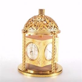 Angelus Hygro Barometer: An Angelus clock/barometer. The etched brass cube contains a Swiss movement clock with Arabic numerals; a Hygro hygrometer; a Celcius dial thermometer and a barometer. The cube rotates underneath a curved, cut-out canopy flanked by rope columns. The piece is marked “Angelus, Fifteen 15 Jewels” to the bottom.