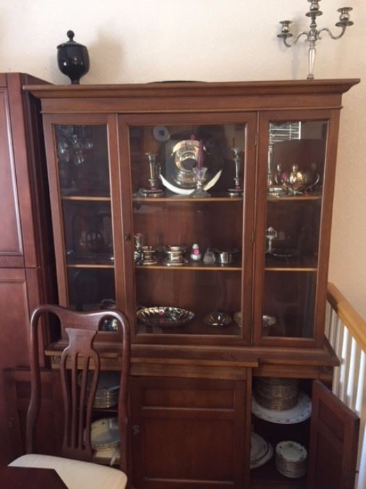 China hutch with china sets inside, plus silver and silver-plate dishes and serving pieces.