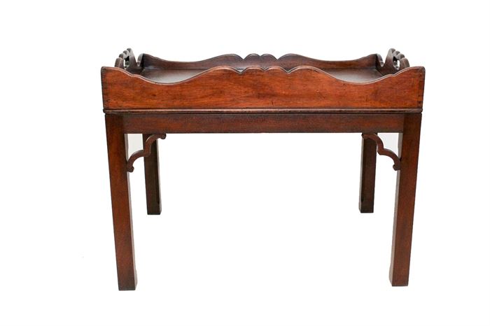 Antique Butler’s Tray Coffee Table: An antique butler’s tray coffee table. This walnut table features scalloped asymmetrical side rails, pierced hand-holds, and decorative corbel trim. It is raised on square legs with fluted detail to the inner edge.