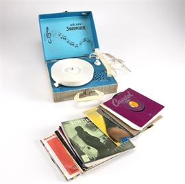 Portable Record Player and Vintage 45RPM Records: A portable record player and 45 RPM records. The record player is a Swinger SP 5 from the company DeJay, and featured a closable lid and handle for ease of transportation. The record assortment is composed of twenty-one records of various popular singles from the time of the creation including Lazy Sunday by The Small Faces,Get Together by The Youngbloods, Atomic Dog by George Clinton and more. Nearly all of the records come with the original sleeves.