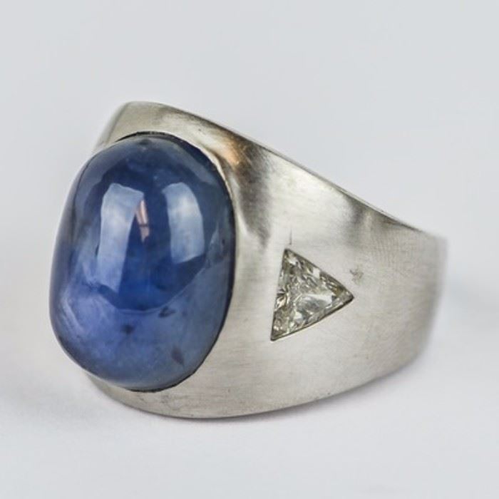Men's 18K White Gold, Star Sapphire, and 1.00 CTW Diamond Ring: A men’s 18K white gold ring featuring one center star sapphire oval cabochon flanked by flush set trillion cut diamond side stones with a total approximate carat weight of 1.00 ctw.