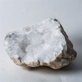 Quartz Geode: A quartz geode. This geode is encrusted along the inside with small semi-transparent crystal quartz points. The exterior of the rock is rough and unpolished.