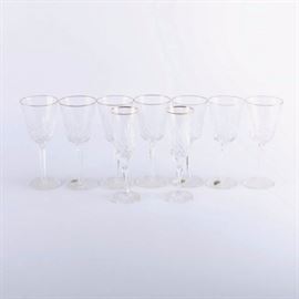 Waterford and Rogaska Crystal Glasses: A group of crystal glasses. This selection includes nine Waterford wine glasses and two Rogaska champagne flutes. The Waterford pieces feature the Golden Lismore pattern with crisscross and vertical cuts and gold tone trim. The Rogaska glasses feature the Richmond pattern with fan and crisscross cuts and gold tone trim. These pieces are all marked to the undersides of the footed bases.