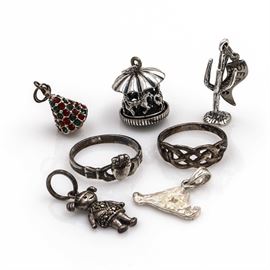 Sterling Silver Jewelry With Marcasite ad Glass Rhinestones: An assortment of sterling silver jewelry with marcasite and glass rhinestones. This group includes two rings and five charms. The rings include a Claddagh ring, and a ring with a woven openwork head. The charms include an articulated carousel, a Christmas tree with glass rhinestones, a girl with pigtails and marcasite rhinestones, a Saguaro cactus with a pennant flag attached that reads, “Sedona Arizona”, and a charm with an abstract shape. Each piece is hallmarked as sterling silver. The total approximate weight inclusive of all non-sterling materials is 0.48 ozt.