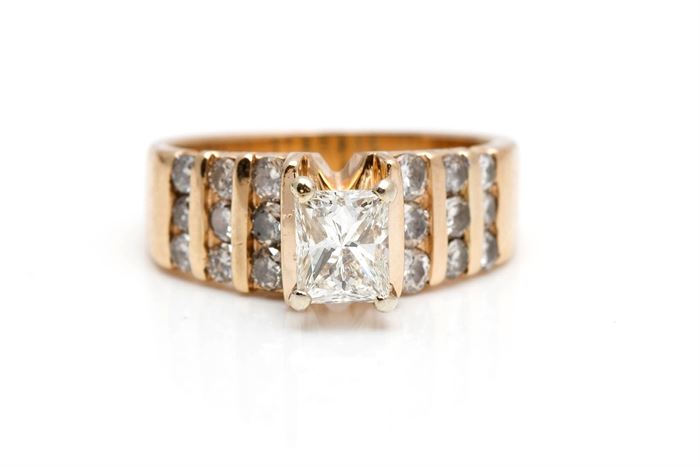 14K Yellow Gold 1.67 CTW Diamond Engagement Ring: A wide yellow gold shank with raised prong set rectangular cut diamond to the center of rows of round cut channel set diamonds to the shank.