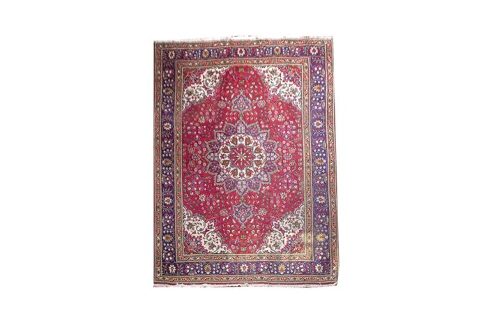 Persian Inspired Area Rug: A machine made Persian inspired area rug. This richly colored rug has a center palmette motif in colors of cream, olive, red and blue. The red background field of the rug has an arabesqued floral and foliate design. 
The guard border of the rug features repeating shah abbasi palmette designs on a blue background. The rug has handwoven cream colored fringe at the ends.
