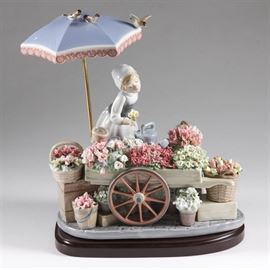 Lladro "Garden of Dreams" Figurine: A signed Lladro porcelain figurine, Garden of Dreams. The hand-painted hard paste porcelain figurine depicts a flower seller at her cart, which is filled with tubs of different flowers, each delicately sculpted of porcelain. The figurine is signed in black ink to the underside “To Nina Martin” and is signed “J Lladro” by D. Jose Puche, an artist who worked on the sculpture, which is numbered 2539. Included with the figurine is a wood display stand. It also comes with a framed certificate of authenticity.