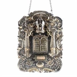 19th Century Sterling Silver Russian Torah Shield: An astonishing example of late 19th century Russian Judaica, a Torah shield in sterling silver with worn parcel gilding. The hand wrought plate displays scrolled foliate and floral detailing to the shaped edges, tapered columns as well as the lions of Judah flanking a dimensional crown with three bells and a bird finial. Hinged doors in the center in the form of the ten commandment tablets open to a recess over a slot frame which contains four interchangeable placards engraved for various holidays. 
The Torah ornamental shield is typically made of silver and engraved with Jewish symbols or scriptures. It is attached to a fine chain, and when the Sefer Torah is closed and covered, the breastplate hangs from the Atzei Chaim over the front of the mantel.

In the ritual function of the synagogue, the Sefer Torah is ornamented with a fitted vestment and either a silver Torah crown or finials and shield. The use of either associates the Tora