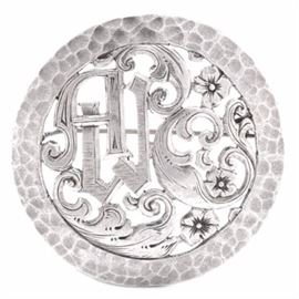 Jugendstil Style Silver Handcrafted Brooch: A round coin silver European brooch with openwork and hammered detail. The center design incorporates the monogram “AW” with scrolling foliate and floral detail typical of the Art Nouveau period. The reverse of the piece is stamped “900, PALA” and “HANDARBEIT” indicating in German that it is handcrafted. The total approximate weight is 0.35 ozt.