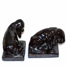 Rookwood Pottery Hound Dog Bookends: A pair of 1928 Rookwood pottery hound dog bookends. The hound dogs have a dark brown gloss glaze and feature charming hound dogs in a seated position over a rectangular base. Designed by Louise Abel. Rookwood flame mark, mold number and date mark to base.