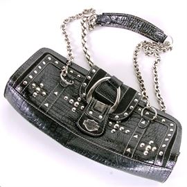 Harley-Davidson Black Leather Bag: A Harley-Davidson black leather purse. The bag features an alligator skin texture with suede accents, silver tone round and triangular stud details and a flap with a large silver tone ring held in place with a leather snap closure marked with a metal Harley-Davidson tag. Two sets of chains on rings are connected to a leather shoulder strap. The purse has a zipper closure. Inside, it features a single compartment with slots for cards and other small items.