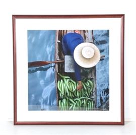 Emerse Limited Edition Digital Print "Aubergine": A limited edition digital print in color titled Aubergine by Emerse. This photograph features a barefooted person kneeling in a wooden boat with an oar sitting across their lap, a wide brimmed hat on their head, and arm reaching into a pile of green gourds. This piece is numbered “14/250”. It is presented behind a white mat behind glass in a wood frame.