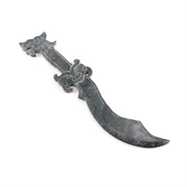 Serpentine Chinese Stone Knife: A Chinese carved serpentine stone knife. The knife features a dragon head pommel, cross hatch carved handle and scrolled guard with a face design ending in a curved scimitar style blade.