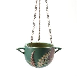 Roseville "Snowberry" Blue Hanging Planter: A circa 1950s Roseville hanging planter in the Snowberry pattern. This piece features a matte blue and red background with ivory, green, and brown embossed snowberries with leaves. The body features arched handles to either side and the rim is pierced with three holes for hanging with hooks attached to a chain. The side of the rim reads, “U.S.A.”