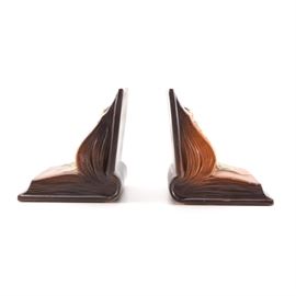 Roseville "Freesia" Bookends: A pair of bookends in the Freesia pattern by Roseville. These pieces are presented as open books with cream freesia flowers with green stems. The relief flowers are placed on an orange and brown ombre background with page details to the sides. The undersides read, “Roseville U.S.A. 15.”