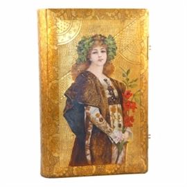 Hand-Painted Art Nouveau German Photograph Album: An attractive, hand-painted Art Nouveau photograph album assembled by C. Feigler Karlsruhe of Germany. The album pages feature gifted edges and windows laid out to display photographs of varying size. They are housed in an embossed cushioned binding having a female figure adorned with a crown of ivy and holding red flowers painted to the center front of cover. A label sticker is affixed to the bottom left of an interior page for “C. Feigler Karlsruhe”.