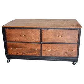 Garage/Workshop Storage and Work Table: A sturdy work bench with ample storage for a garage or workshop. This piece is made of wood and includes an oversize work surface with four extra deep drawers below. Black painted trip highlight the drawer frames. The right side of the piece is painted black with raised panels. Four sturdy rubber casters support the work bench and make it portable.