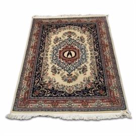 Hand-Knotted Tabriz Area Rug: A hand-knotted Tabriz area rug. This rug features a central black pictorial motif bordered by a floral wreath inside of a red geometric medallion on a cream backdrop. Floral motifs fill the cream colored center as an arabesque pattern fills a black border. A second border with a red ground color is ornamented in floral motifs. Off-white fringe appears to either end of the rug. A label is attached to the rug and is marked, “Genuine Hand Woven Oriental Rug.”