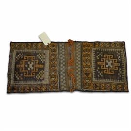 Hand-Knotted Caucasian Saddle Rug: A hand-knotted Caucasian saddle bag. This bag features two identical pieces sewn together. Each piece depicts a geometric central medallion in a gold tone on a brown backdrop. A pattern of geometric shapes depicting ram horns make up the border on a gold tone ground color. There is a flap on one side that opens to reveal a compartment for storage. There is no maker’s mark or label present.