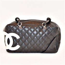 Chanel Ligne Cambon Quilted Bag: A Chanel Ligne Cambon quilted bag. This bowler bag is made of black calfskin leather and features a large version of Chanel’s double C logo in white. It has silver tone hardware, a single pocket on the exterior, black knotted leather straps and a main Lampo zipper. The interior is lined with a pink logo print material and offers two pencil holders, a cell phone sleeve and an interior pocket with a zipper closure. The serial number is 9512779. A protective storage bag is included.