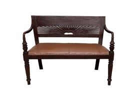 Vintage Wooden Bench: A vintage wooden bench. A gorgeous Louis XVI style mahogany bench seat with a brown leather cushion. This bench features a hand carved backrest in a sunburst motif with a floral trim. The arms are a curving piece of wood with a carved and turned front leading to reeded tapered legs. The padded brown leather seat is accented with criss-cross lacing and anchored with brass rivets.