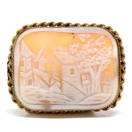Victorian Gold Filled Carved Shell Cameo Brooch: A antique Victorian gold filled brooch featuring a carved shell cameo depicting a village of houses with a tree and a woman standing in the center.