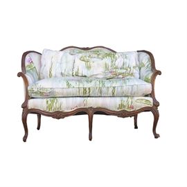 Louis XV Country Style Settee: A Louis XV country style settee. It features a cream cotton upholstery featuring a pastel green and pink floral print that resembles a watercolor painting to the front as well as the removable seat and back cushions. The back and sides have a green and white plaid upholstery. This settee features a carved walnut frame with a curved crest and apron, rolled arms, and five cabriole legs.
