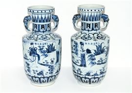 Duo of White and Blue Asian Motif Vases: A duo of white and blue ceramic vases with an Asian motif. Each hand-painted vase has a narrow neck and two handles.