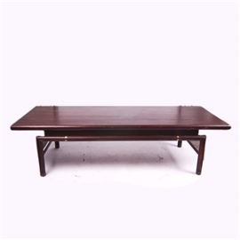 Mid Century Modern Coffee Table: A Mid-Century Modern wooden coffee table. This piece is featured in a cherry stain. It consists of a rectangular surface top with a simplistic base with gold tone metal ornaments and straight legs.