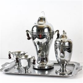 Vintage Faberware Chrome Coffee Service: A vintage Faberware chrome coffee service. This bright chrome set includes a percolator, lidded coffee pot, sugar and creamer atop a rectangular serving tray with cut out handles. The percolator, sugar and creamer have wooden handles. The coffee pot and percolator are embellished with an etched swag motif. They are marked to the reverse Faberware, Brooklyn. This set is also marked “number 100”.
