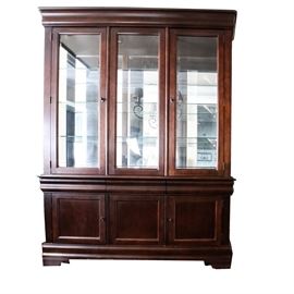 Broyhill "Maison Lenoir" China Cabinet: A Broyhill Maison Lenoir china cabinet. Behind the cabinets two beveled glass doors are three rows of glass shelves encased in a heavy, dark stained wood. The cabinet sits atop three shallow drawers with interior felt accents. Below the drawers is a cabinet with doors to either side of the case. The cabinet is made of hardwood with dove tailed joints and drawer guides. This piece matches items 17COL054-003, 17COL054-004, 17COL054-005 in this sale.