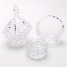 Crystal Bon Bon Bowls and Ashtray: A group of crystal décor. This includes a basket bon bon dish with coin shape detailing with foliate designs to the body. There is also a footed candy bowl with hobnail and pinwheel detailing that has a tall lid with a tapering faceted finial handle. These are accompanied by an ashtray with intricate cut ornamentation and two cigarette rests. No discernible maker’s mark was found.