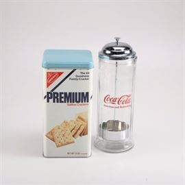Vintage Coca Cola Straw Dispenser And Nabisco Cracker Tin: A vintage Coca-Cola straw dispenser and Nabisco cracker tin. A TableCraft CC322 Coca-Cola straw dispenser features a clear glass body with red script logo and an internal chrome holder with a center lift post attached to the dome lid. The underside is pressed, " © 1992 The Coca-Cola Company. All rights reserved". The 1978 Nabisco “Premium Saltine Crackers” tin features a square design with blue lid and painted packaging label on the body.