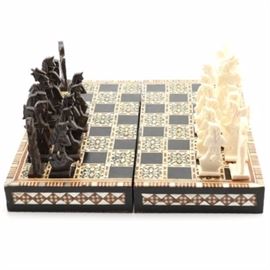 Carved Bone Chess Set with Mother of Pearl Inlaid Board: A carved bone chess set with a board inlaid with mother of pearl. This set features black and white chess pieces carved from bone with red felt on the underside of each piece. The set comes with a hinged wooden board inlaid with mother of pearl featuring a checkerboard with starburst-like squares on one side; a diamond shaped geometric pattern on the sides; and a backgammon board on the interior.