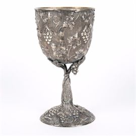 Large Sterling Silver Grapevine Motif Chalice: A large sterling silver chalice. The chalice is adorned with hand worked repousse and hand chased floral grape and vine motif that twist down the stem to a defined base. The chalice is marked with a “925” to the bottom of the base and weighs approximately 19.010 ozt.