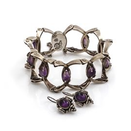 Sterling Silver Amethyst Bracelet and Earrings: A sterling silver amethyst bracelet and earrings. This set features a pair of hook back earrings with geometric bodies housing bezel set amethysts, and a hidden box tab pierced geometric linked bracelet with prong set amethyst stones.